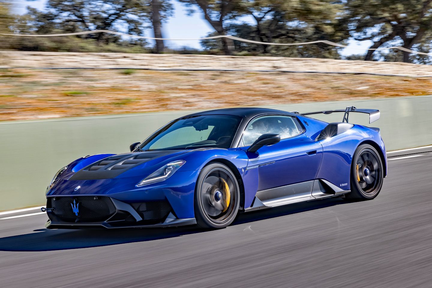 Blue Maserati sports car racing on a track, yellow brake calipers visible and a large rear wing in the back.