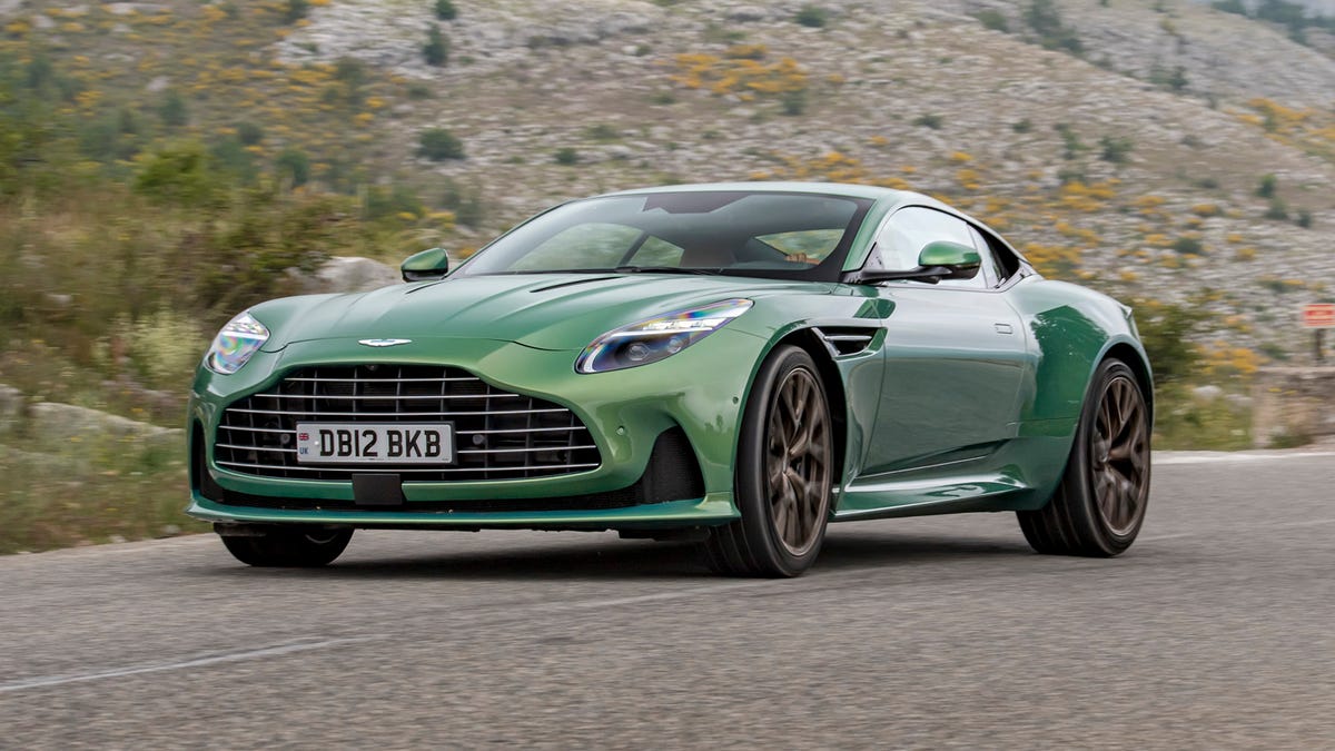 Green Aston Martin on a winding mountain road, front 3/4 view showcasing the grille and sporty design