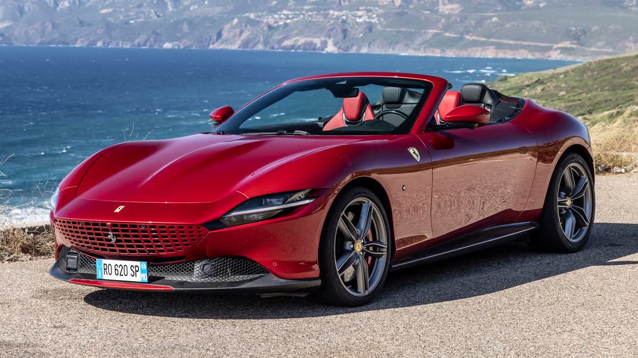 Red Ferrari Portofino convertible parked on a coastal road with the sea and cliffs in the background, open-top luxury sports car