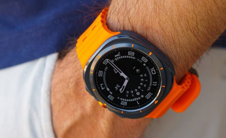 Wristwatch with a black dial and orange silicone strap on a hairy wrist, close-up shot showing time markings and hands.