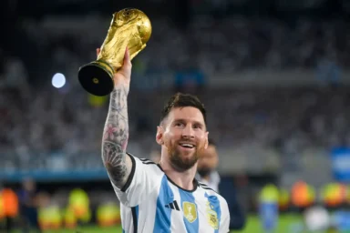 Lionel Messi in Argentina colors lifting the FIFA World Cup trophy in celebration on the pitch.