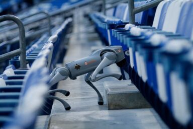 Gray robotic prosthetic leg resting on a concrete step among blue stadium seats, showing joints and foot clearly in focus