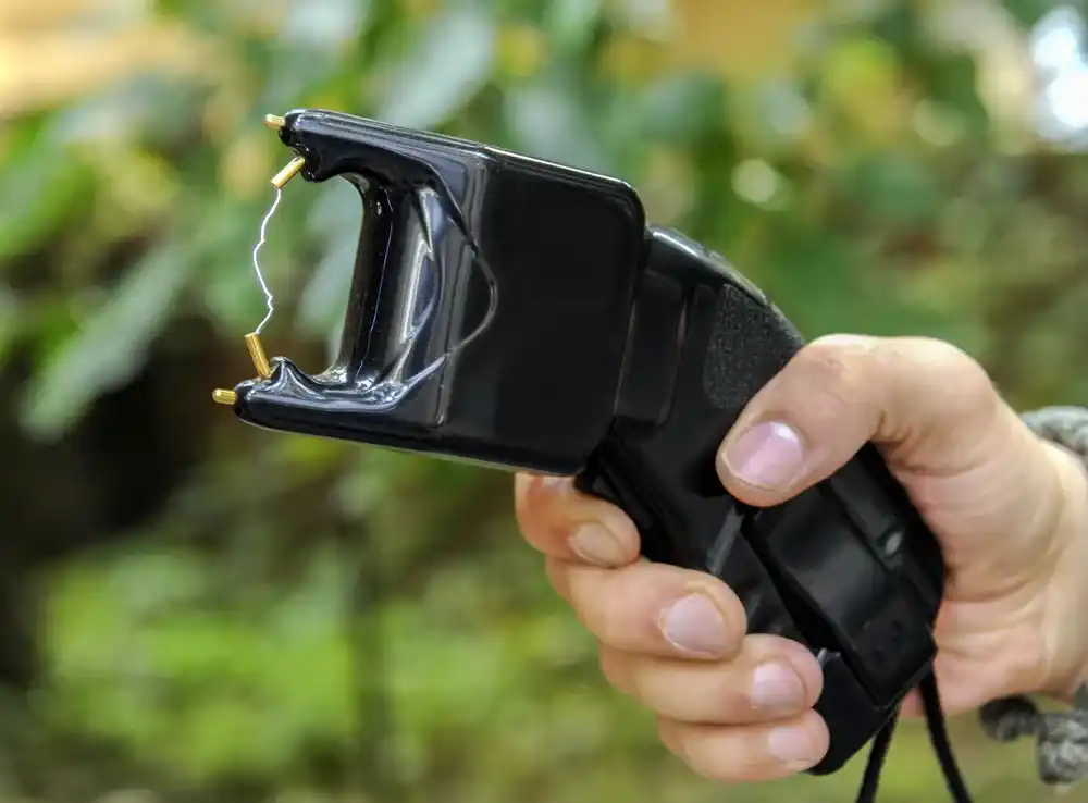 Close-up of a hand gripping a black handheld device with a damaged front exposing small metal pins and a loose wire, outdoors