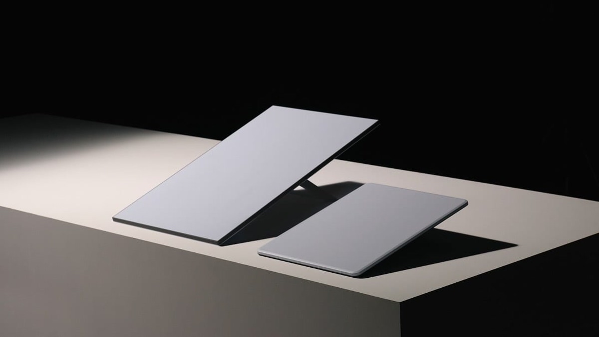 1000049968 Two gray tablets displayed on a white pedestal against a dark background, angled for viewing.
