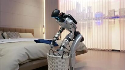 Humanoid robot bending over a white wicker basket in a modern bedroom, reaching inside for laundry.