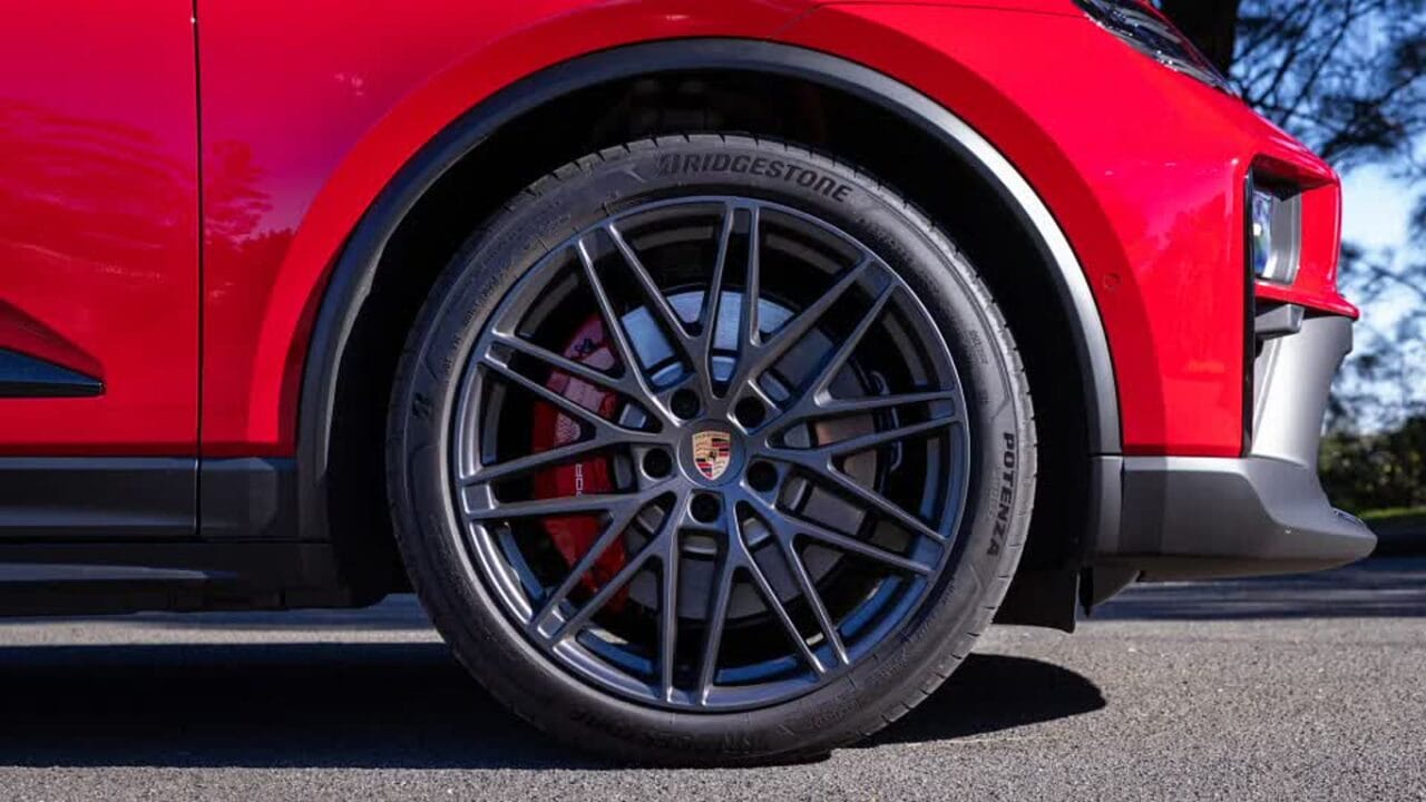 Close-up of a red Porsche wheel with a multi-spoke alloy rim, red brake caliper, and Bridgestone Potenza tire lean against the asphalt.