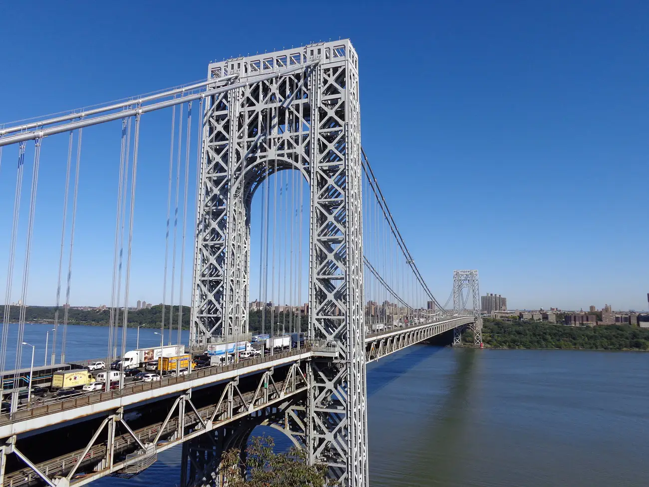 Steel suspension bridge with traffic, spanning a wide river under a clear blue sky.