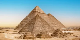 Three ancient pyramids rise from a desert landscape under a bright blue sky at Giza, Egypt.