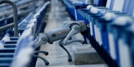 Gray robotic prosthetic leg resting on a concrete step among blue stadium seats, showing joints and foot clearly in focus