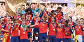 Spain national soccer team celebrates on stage with trophy and gold medals amid confetti and cheering fans.