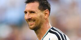 Smiling man in Argentina soccer jersey on the field, sweaty after a match.