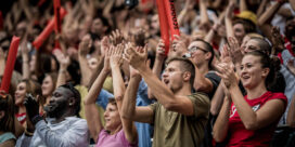 Crowd of cheering spectators in a stadium with hands raised and red inflatables in view